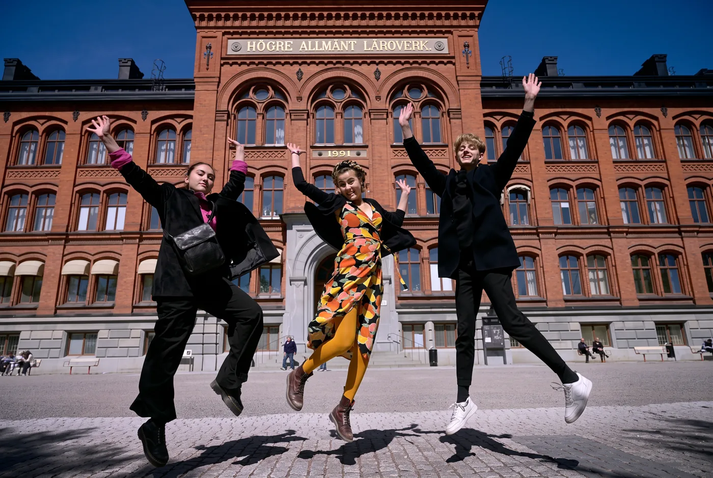 Glada gymnasieelever hoppar framför Södra Latins gymnasium i Stockholm
