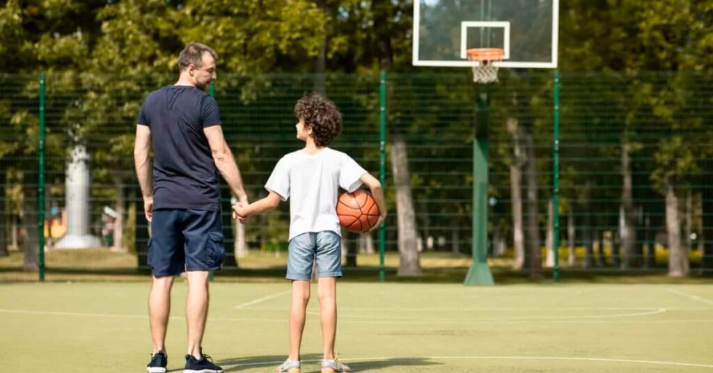 Förälder och barn går tillsammans på en basketplan utomhus