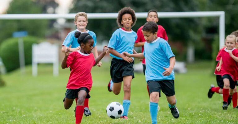 Barn spelar fotboll tillsammans på gräsplan utomhus